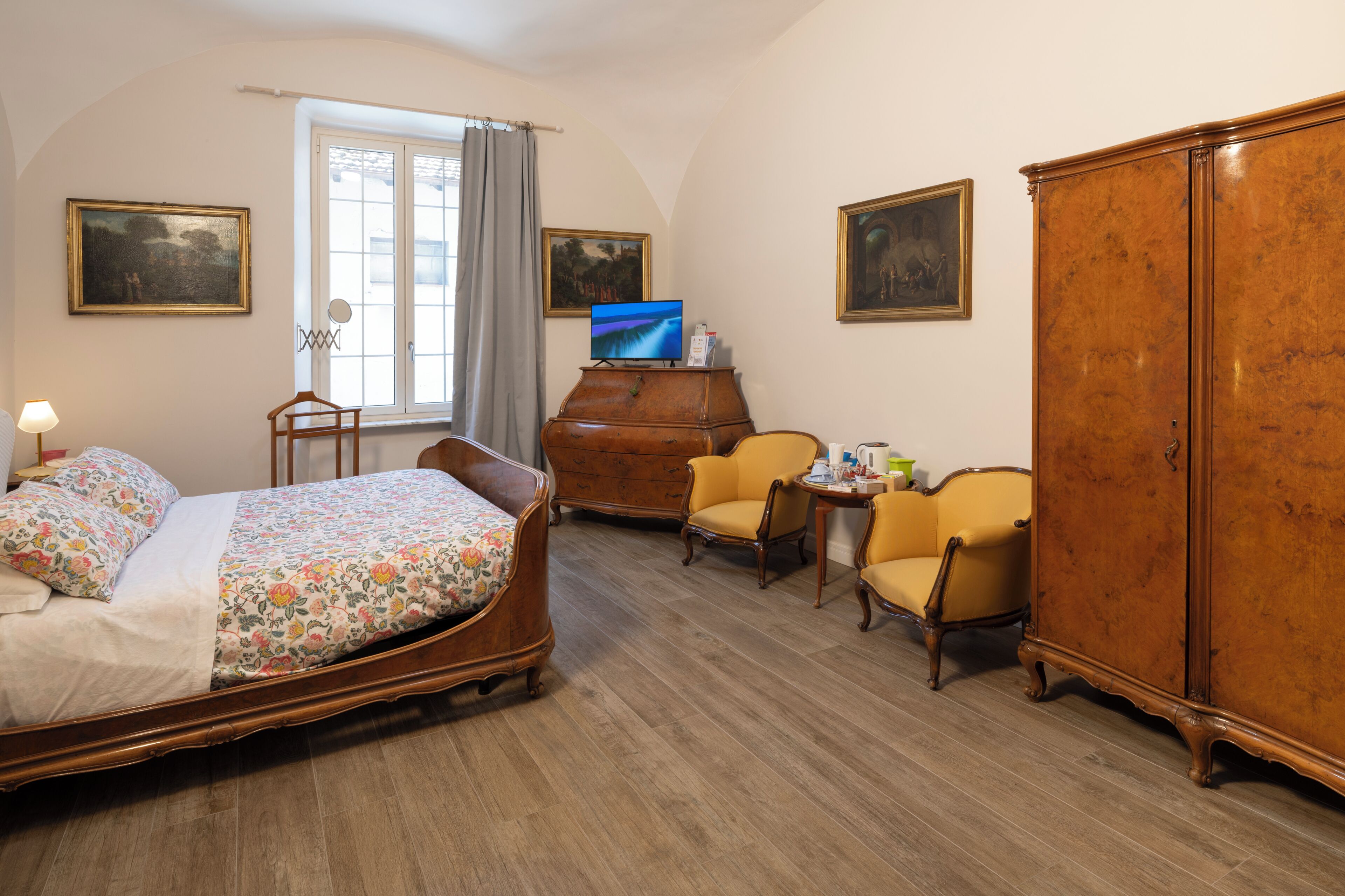 A bedroom with a bed, a dresser, two chairs, a television, and artwork on the walls.