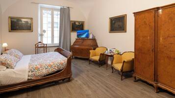 A bedroom with a bed, a dresser, two chairs, a television, and artwork on the walls.