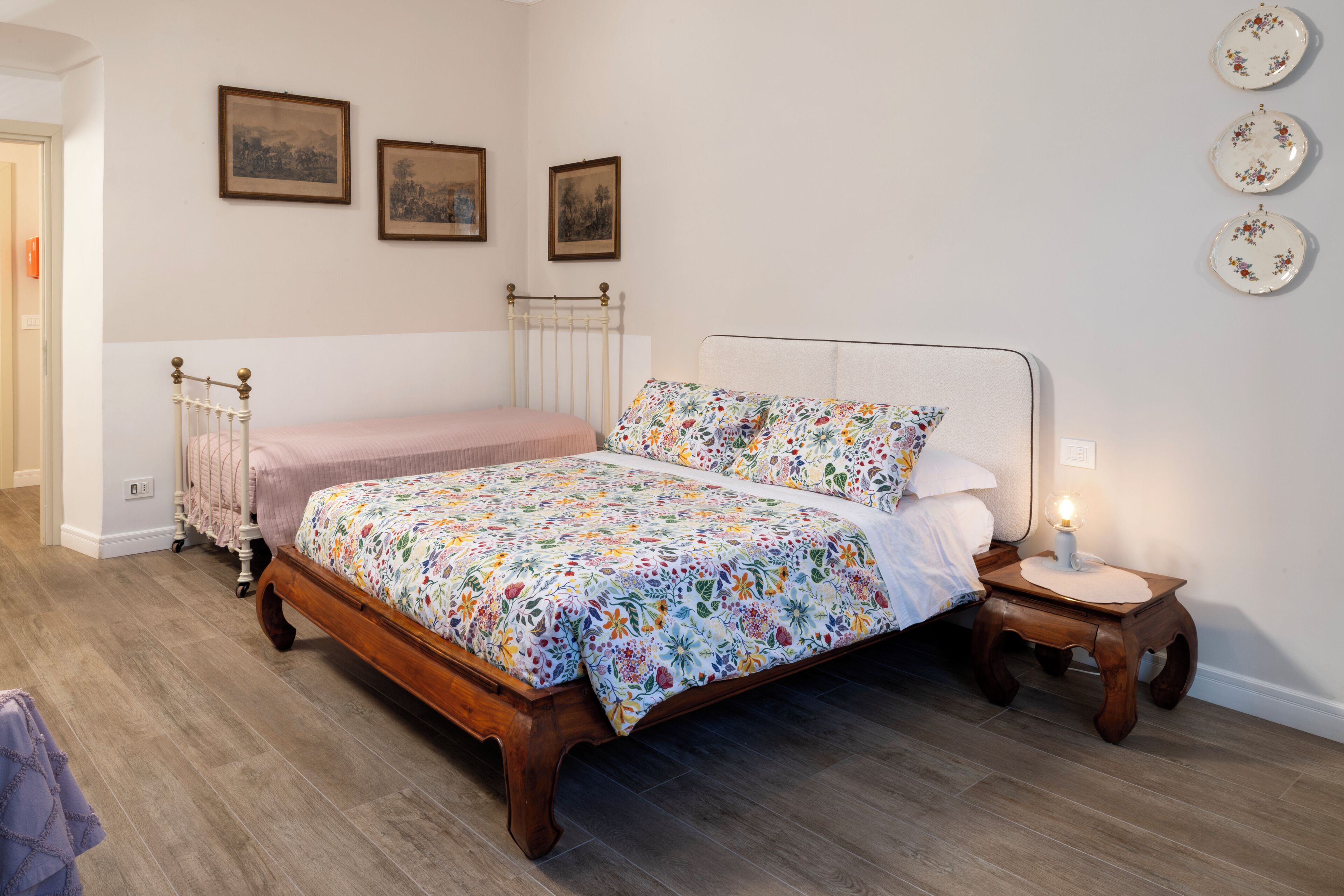 A bedroom with a wooden bed, a bedside table with a lamp, and three framed pictures on the wall.