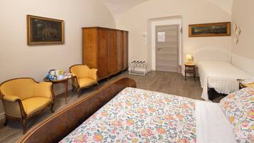 A hotel room with a bed, two armchairs, a wooden wardrobe, a small table with a lamp, and a door leading to another room.