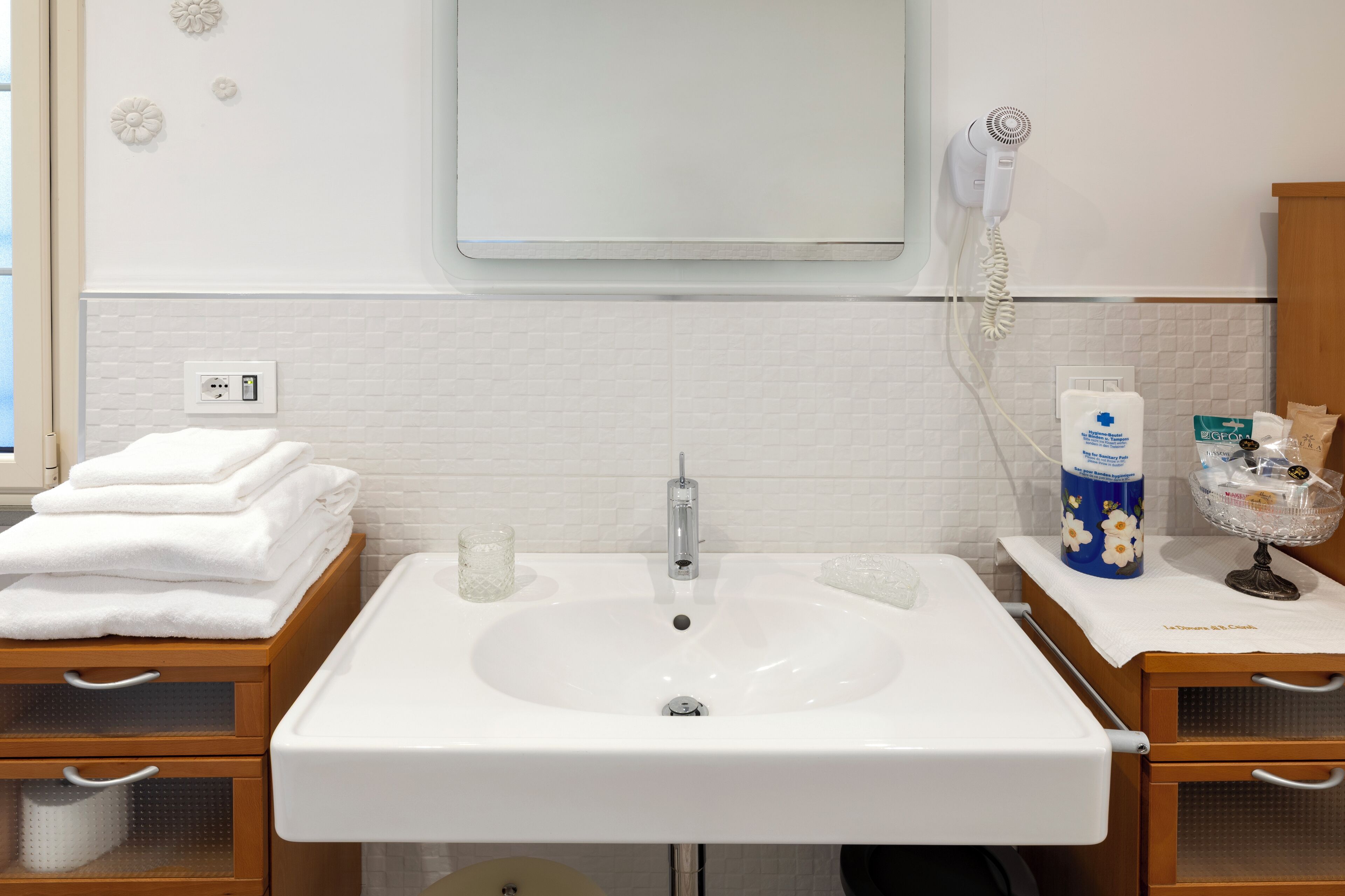 Une salle de bain avec un lavabo blanc, un miroir au-dessus, un sèche-cheveux fixé au mur et un porte-serviettes avec des serviettes pliées.