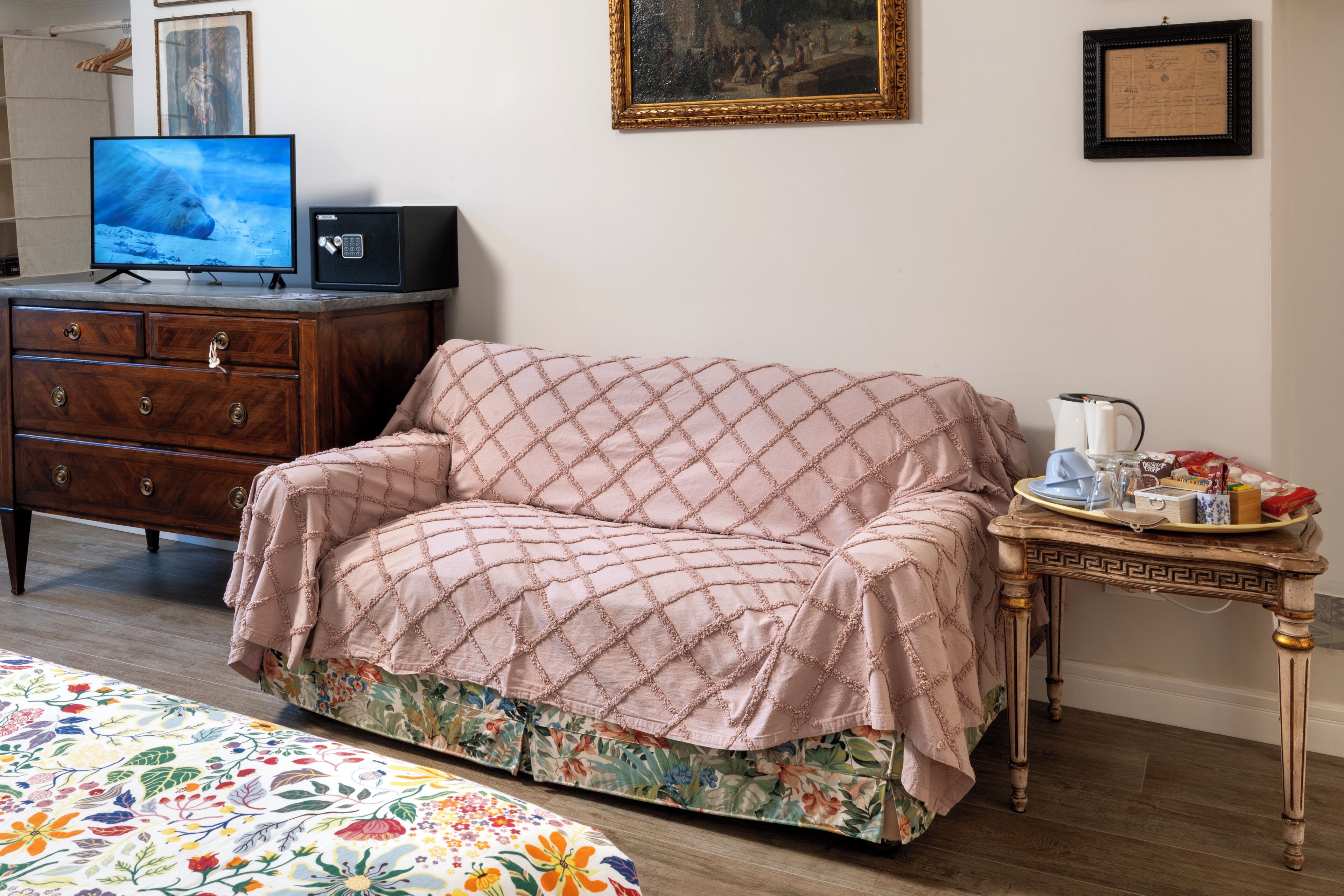 Una habitación con cómoda de madera, televisor, sofá acolchado, colcha con estampado floral y una mesita con bandeja.