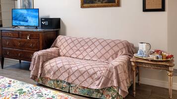 Una habitación con cómoda de madera, televisor, sofá acolchado, colcha con estampado floral y una mesita con bandeja.