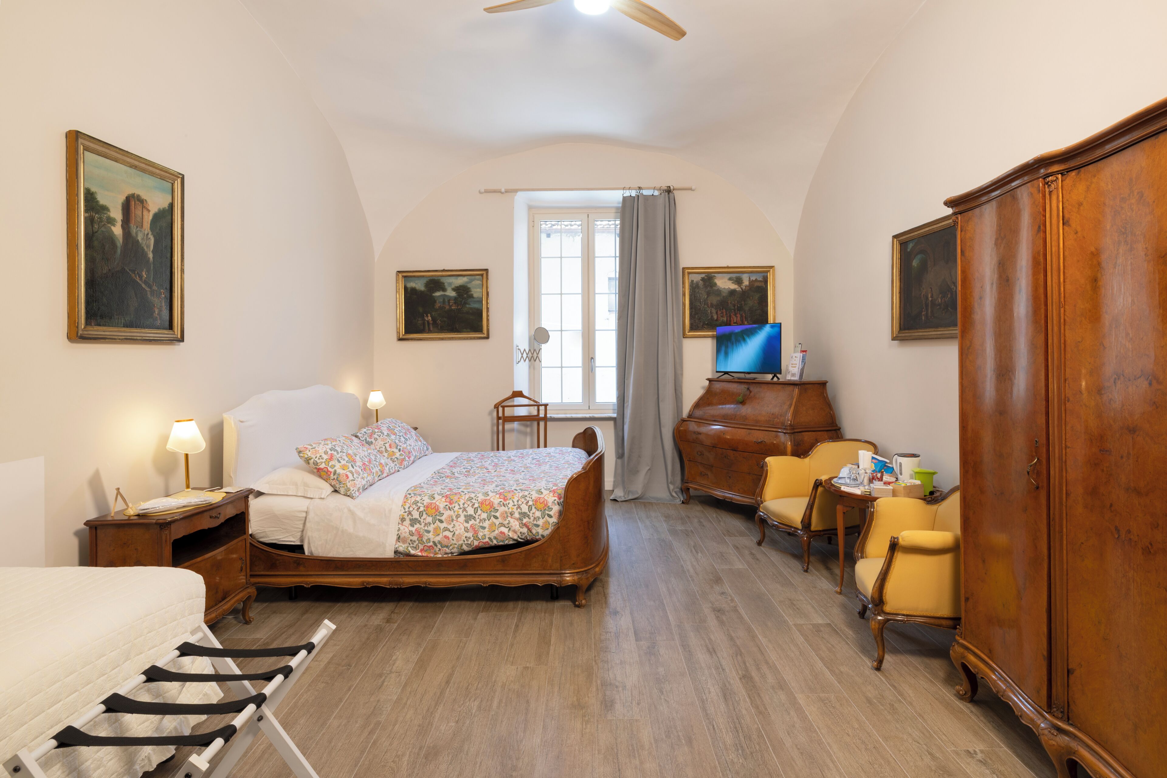 Een slaapkamer met een bed, een dressoir, een televisie en een raam met gordijnen.