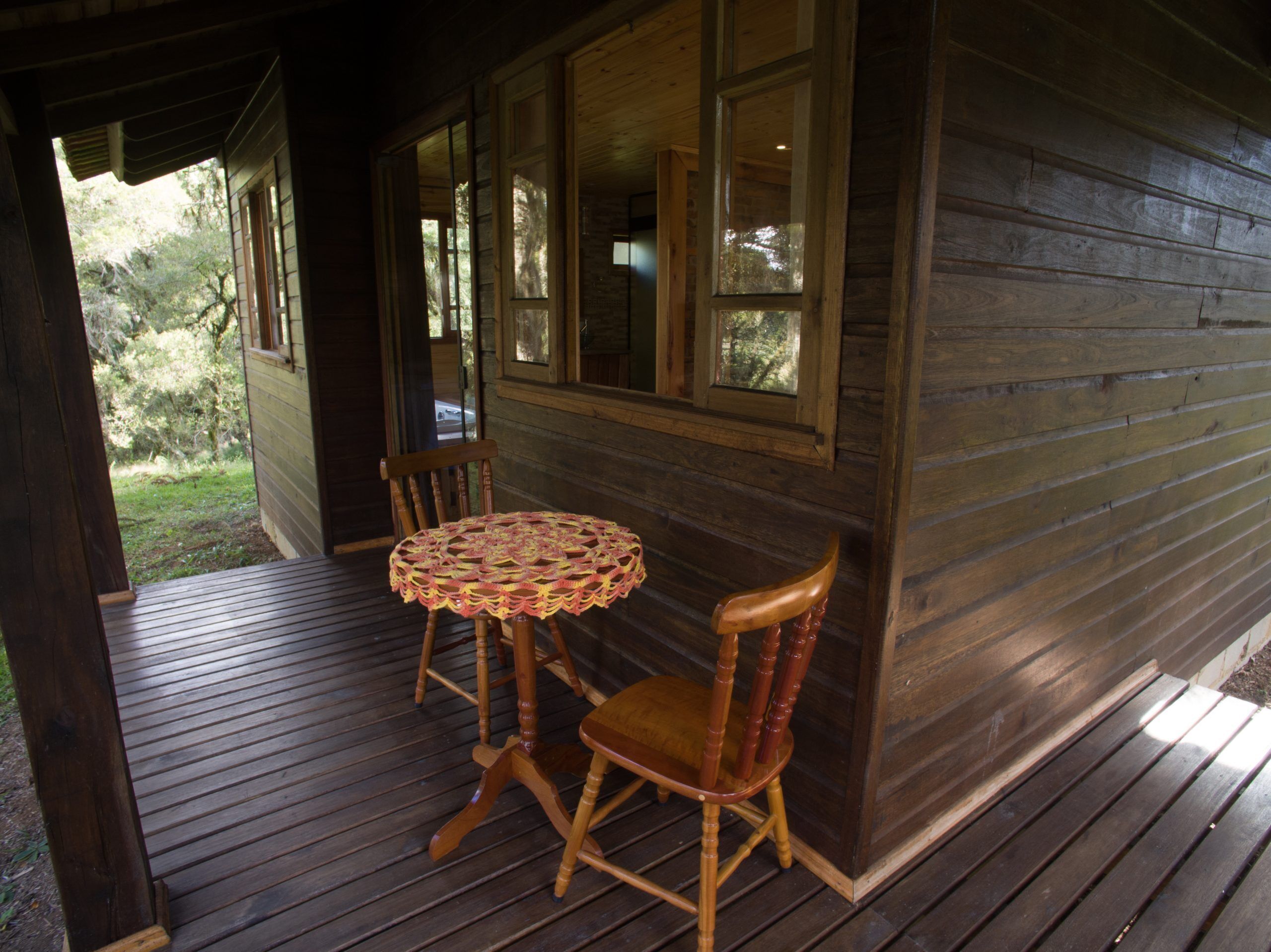A wooden cabin with a porch, a round table, and two chairs.