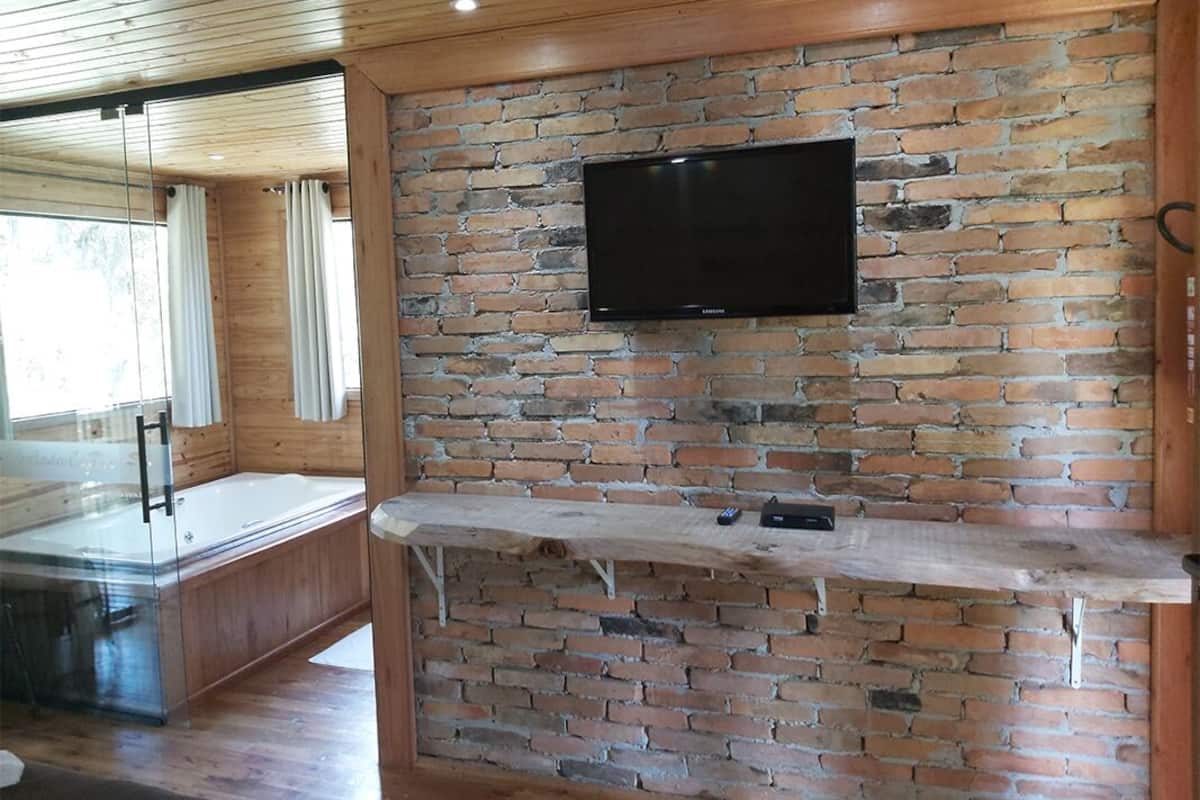 Quarto com parede de tijolos, televisão montada e banco de madeira.