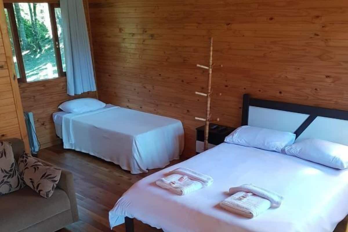 Uma cabana de madeira com duas camas, um sofá e uma janela com cortinas.