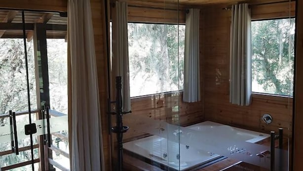 Une cabane en bois dotée d’un jacuzzi à moitié vitré, de grandes fenêtres et d’une terrasse en bois.