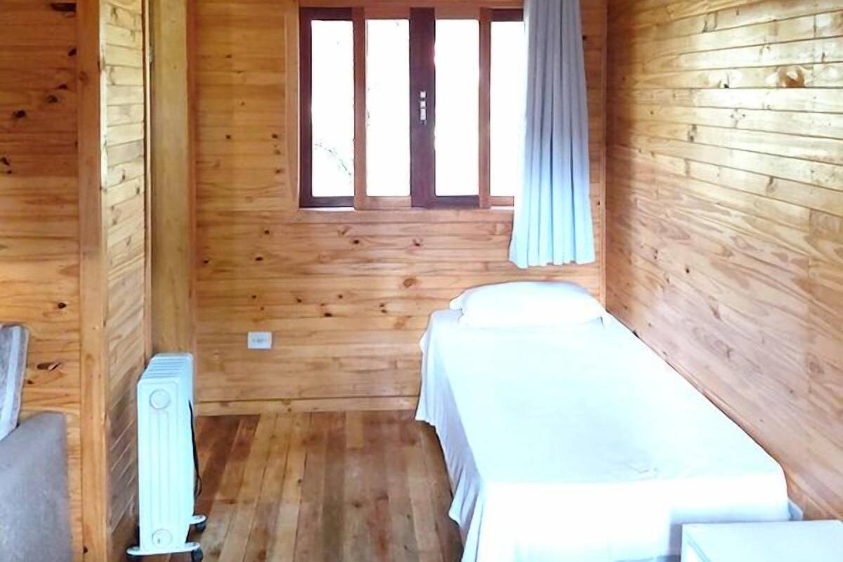 Quarto de cabana de madeira com duas camas, uma janela com cortinas e um radiador.