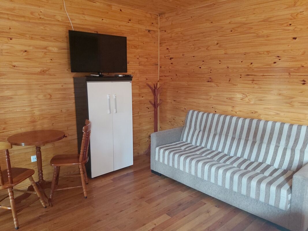 Una habitación con paneles de madera, un sofá, un televisor sobre un mueble bajo y una mesa de comedor con sillas.