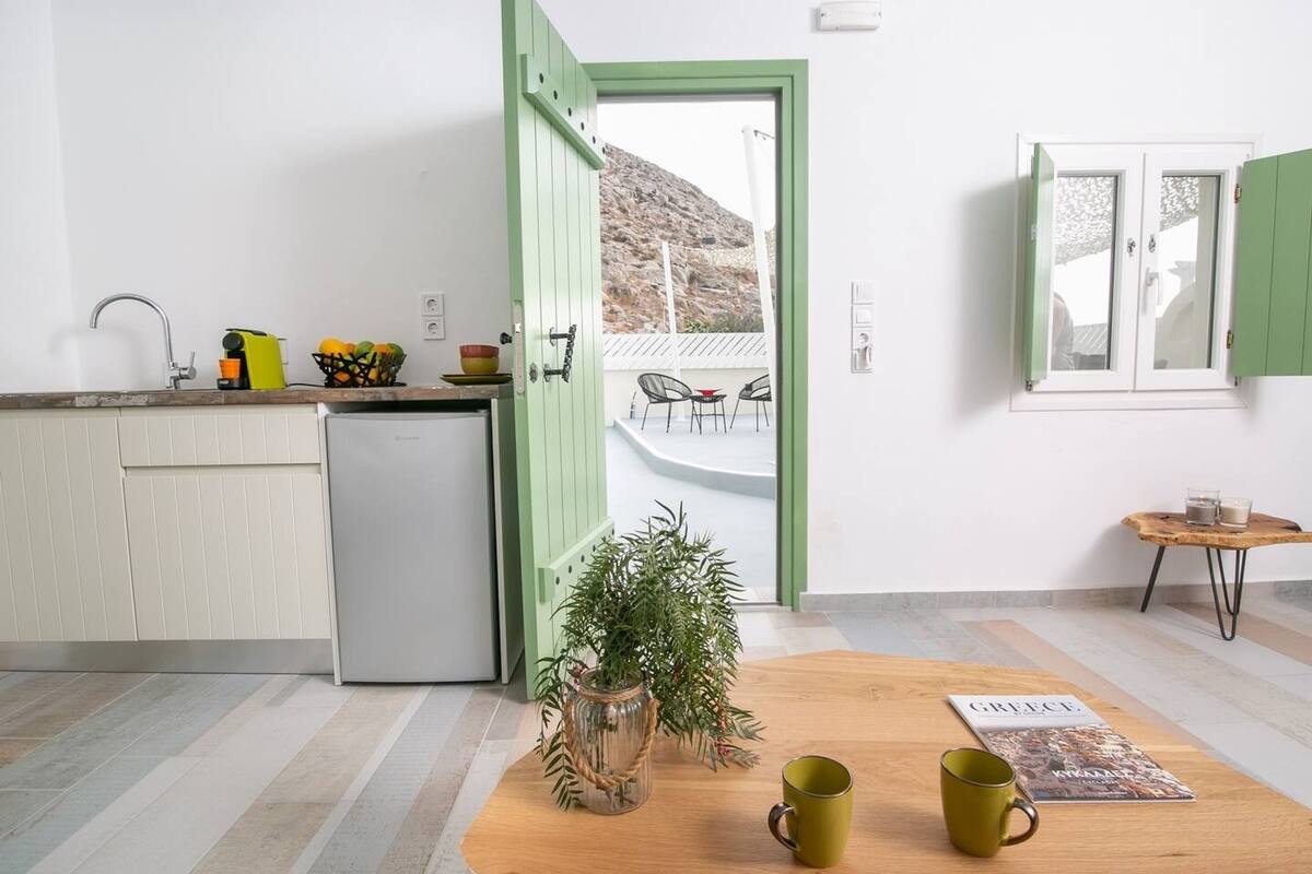 A modern kitchen with a built-in refrigerator, a wooden table with a magazine and a mug, and a view of a balcony with chairs.