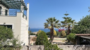 A coastal building with a balcony overlooking the sea, surrounded by palm trees and other vegetation. - Sylvia s House at Vagia (Aegina)
