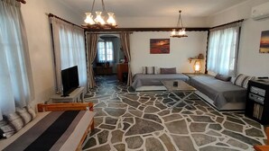 A cozy living room with a stone-patterned floor, a sofa set, a television, and a vintage radio. - Sylvia s House at Vagia (Aegina)