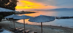 Uma praia com guarda-sóis de palha e vista para o mar ao pôr do sol.