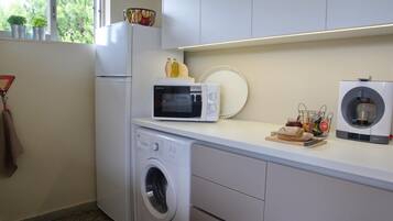 A compact kitchen with a washing machine, a microwave, and a coffee machine.