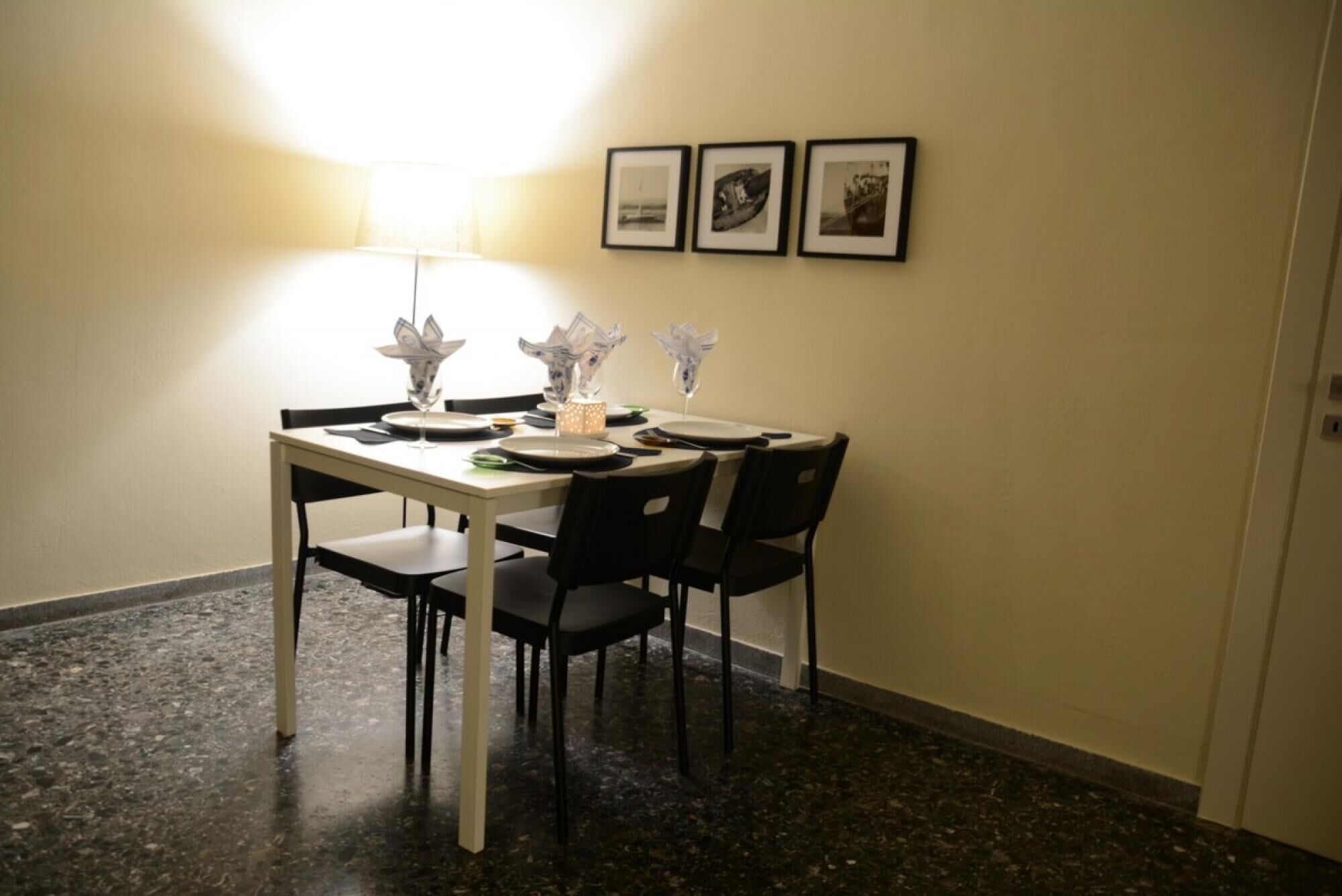 A dining area with a table set for four, chairs, a lamp, and framed pictures on the wall.