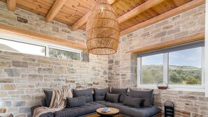 Un salon chaleureux avec un mur en pierre, une grande fenêtre, un plafond en bois et un luminaire en fibres tressées.