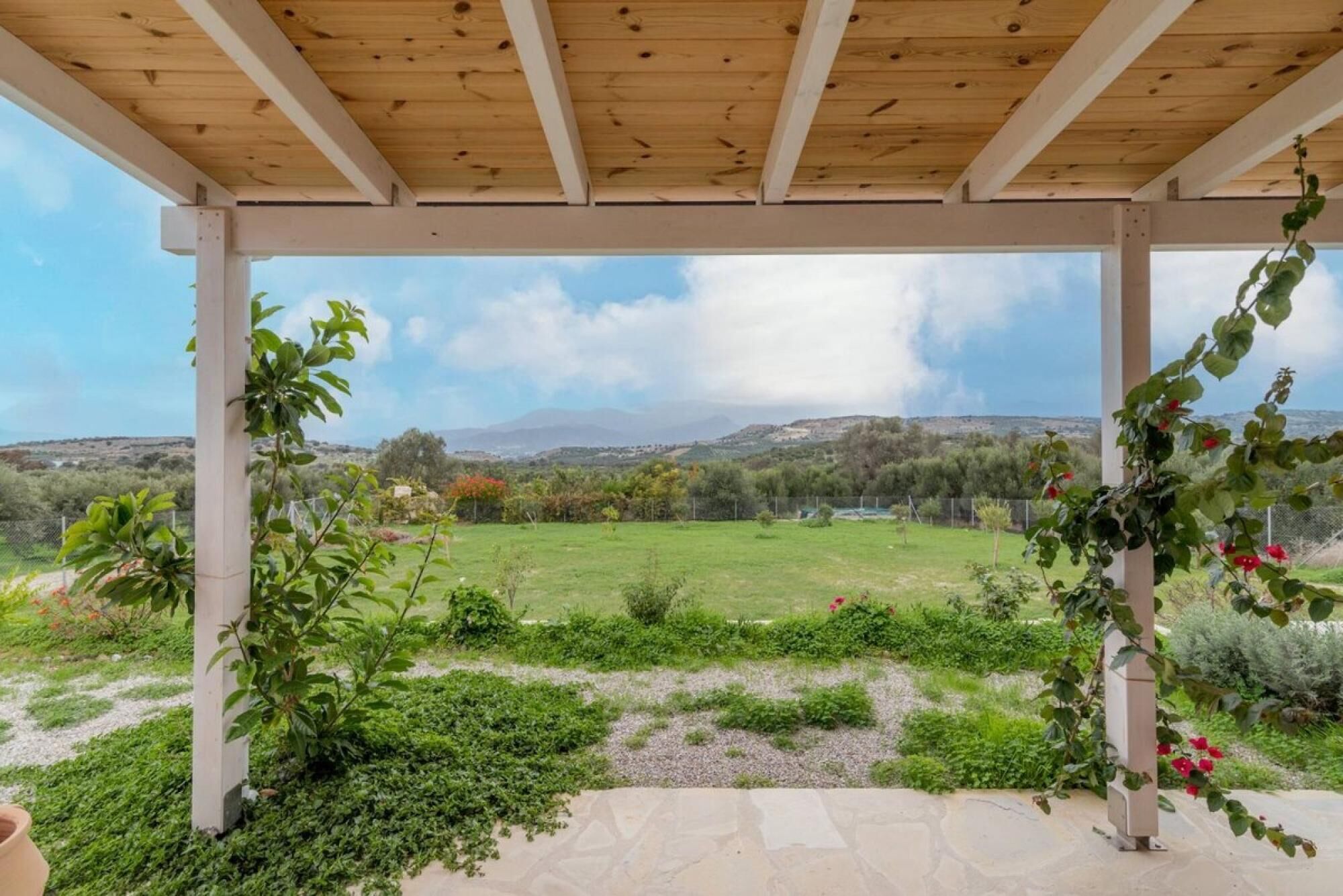 A covered patio with a view of a grassy field and distant hills.