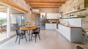 Une cuisine moderne avec des murs en pierre, des poutres en bois au plafond et un grand îlot central doté d’un évier et d’un plan de travail.