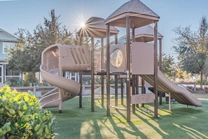 Une aire de jeux avec un toboggan, une zone d’escalade et une cabane couverte.
