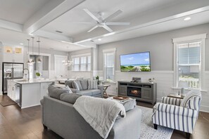 Un salon moderne avec un canapé gris, une cheminée, un téléviseur et un coin repas.