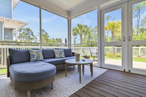 A covered outdoor seating area with a sofa and a small table, a wooden deck, and a view of the surrounding greenery. - 3,000+ Sq Ft! Golf Cart & 6 Bikes! Walk to 2 Pools! 3 King Suites and Bunk Room! ~ Unwined at Naturewalk on 30A (Santa Rosa Beach)
