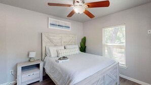 A bedroom with a bed, a nightstand, a ceiling fan, a window, and a plant.