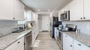 A modern kitchen with white cabinets, granite countertops, stainless steel appliances, and a tiled backsplash.