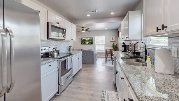 A modern kitchen with stainless steel appliances, white cabinetry, and a granite countertop.