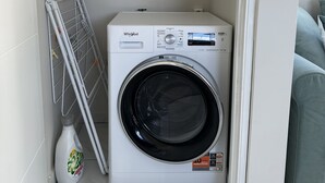 Eine kompakte, weiße Whirlpool Waschmaschine und Trocknerkombination in einem kleinen Waschraum, mit einem Wäscheständer aus Metall und einer Flasche Ariel Waschmittel.