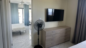 Ein Hotelzimmer mit Bett, Kommode, Fernseher, Standventilator und einer Tür zu einem anderen Raum.