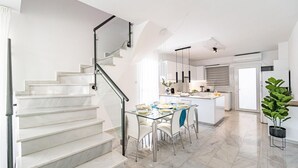 Une cuisine moderne dotée d’un îlot central, d’un coin repas avec une table en verre et d’un escalier avec une rampe en verre.