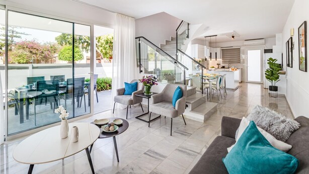 Un salon moderne doté d’un espace repas avec une table en verre, d’un escalier menant à la cuisine et offrant une vue sur l’extérieur.