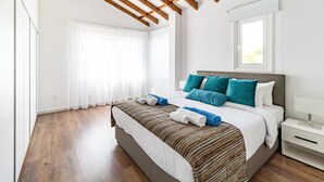 Une chambre à coucher moderne avec un grand lit, des poutres en bois au plafond et une fenêtre laissant entrer la lumière naturelle.