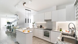Une cuisine moderne avec des meubles blancs, un îlot central doté d’un plan de travail noir et un évier en acier inoxydable.