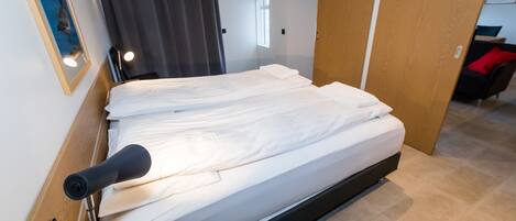 A neatly made bed with white linens, a bedside table with a lamp, and a door leading to another room.