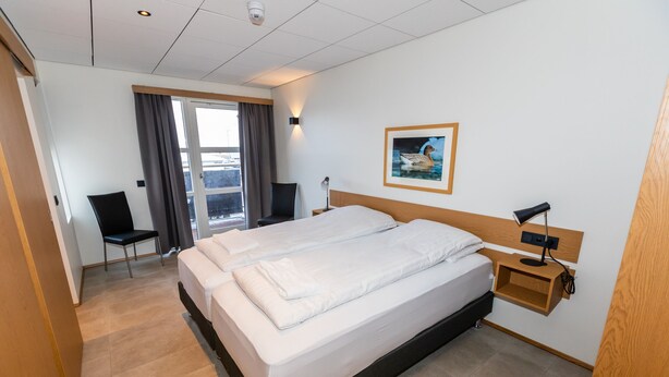 Habitación de hotel con una cama grande, un escritorio, una silla y una ventana con cortinas.