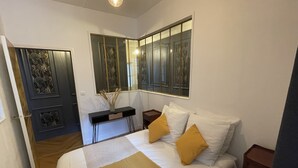 Un dormitorio con cama, mesitas de noche, un espejo y una puerta que da a otra habitación.