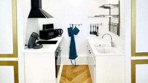 Cocina compacta con muebles blancos, extractor de aire negro, cafetera y toalla colgando.