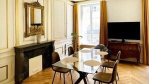 Un comedor con mesa de vidrio, sillas, chimenea, televisor y cortinas.