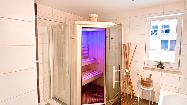 Ein modernes Badezimmer mit einer gläsernen Sauna, einem Holzschrank und einem Fenster mit Blick auf Gebäude.