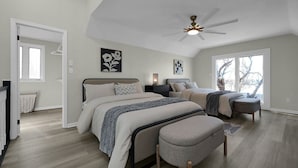 Una camera da letto con un letto grande, un letto più piccolo, un comodino, una sedia e una ventola a soffitto. Si vede una finestra con vista sugli alberi.