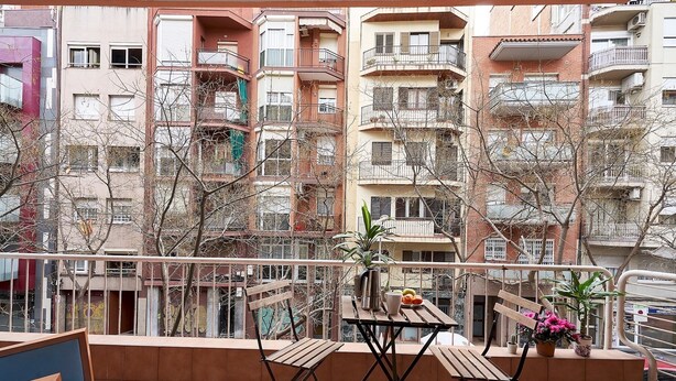 A balcony with a wooden table and chairs, surrounded by buildings with balconies and windows. - San Fructuoso ·  - Three Bedroom Apartment, Sleeps 5 (Barcelona)