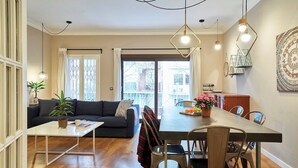 A dining area with a wooden table and chairs, a sofa, and a small table with a plant and books. - San Fructuoso ·  - Three Bedroom Apartment, Sleeps 5 (Barcelona)