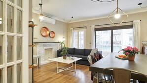 A modern living room with a fireplace, a dining area with a table and chairs, and large windows offering a view of the city. - San Fructuoso ·  - Three Bedroom Apartment, Sleeps 5 (Barcelona)