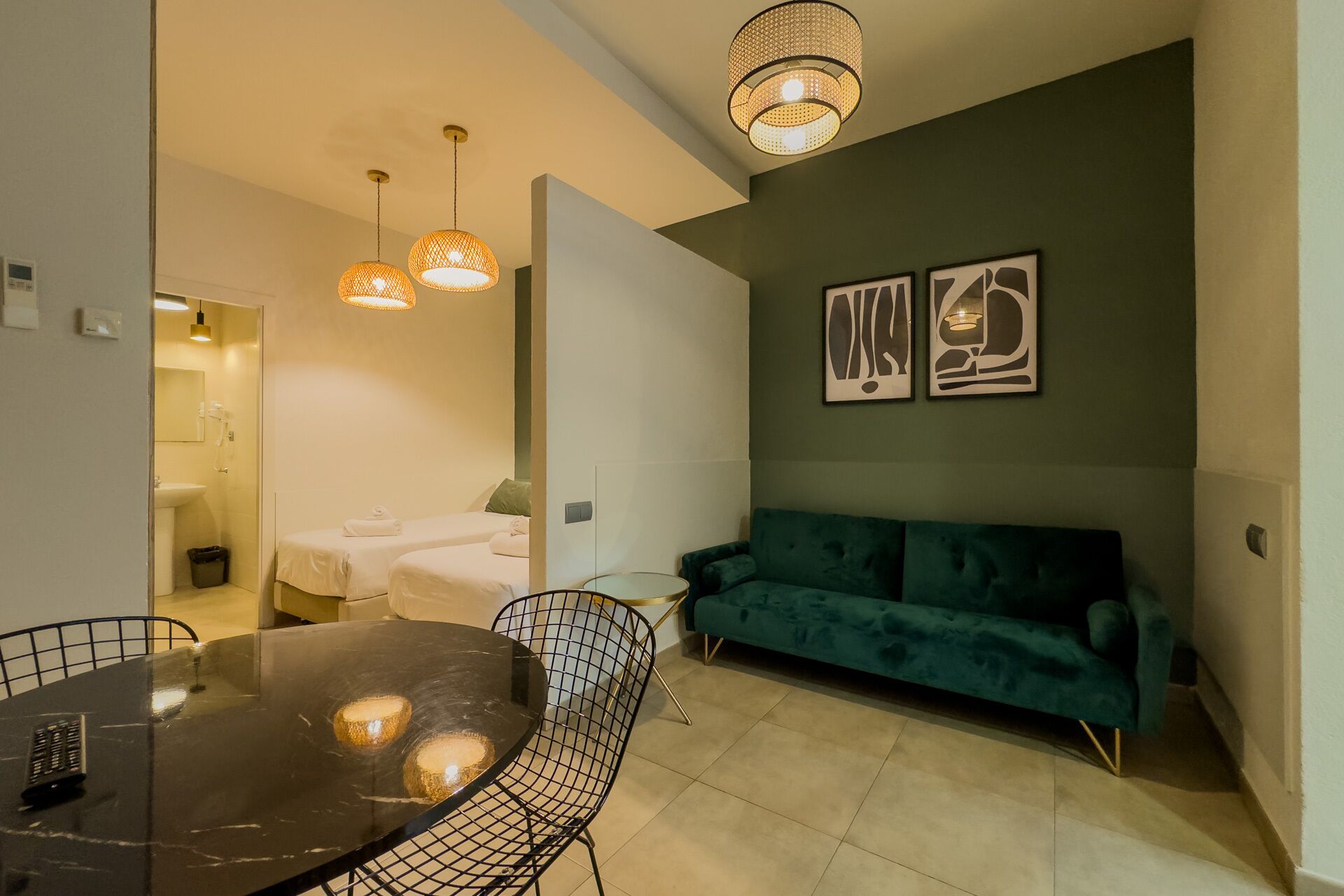 A modern living room with a green sofa, a round dining table with chairs, and pendant lighting.