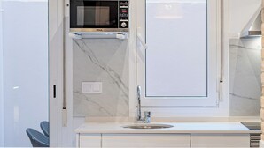 A modern kitchen with a built-in microwave, a large window, and a bar area with metal chairs. - TIinent Flomesta 2110 (Barcelona)