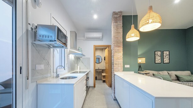 A modern kitchen with white cabinetry, a built-in microwave, and a large island. There is a brick accent wall and a hanging light fixture. - TIinent Flomesta 2110 (Barcelona)