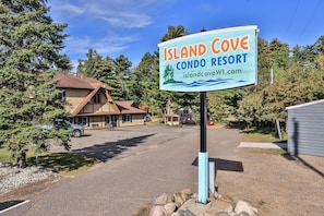 A sign for Island Cove Condo Resort with a website address, surrounded by trees and a building.