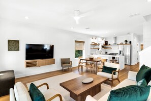 Un salon moderne doté d’un téléviseur à écran plat, de sièges confortables et d’un coin cuisine avec des meubles blancs et des appareils en acier inoxydable.